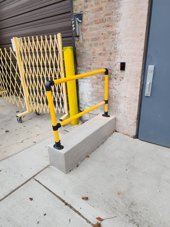 Gelbes Schutzgeländer aus Stahlrohr vor Gebäudeeingang mit Sicherheitsmarkierung